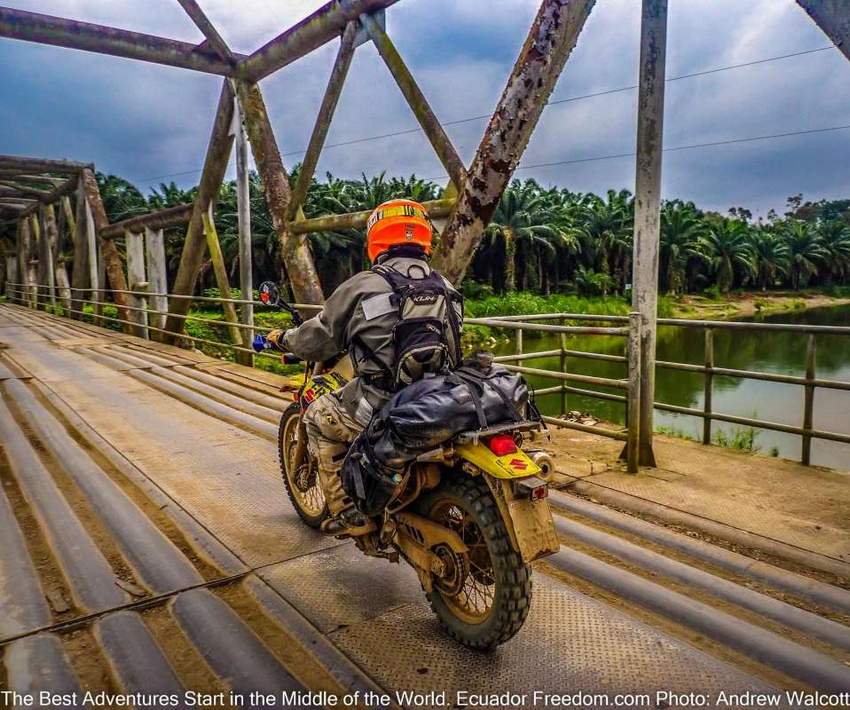 dual sport motorcyclist crossing metal bridge in rural ecuador