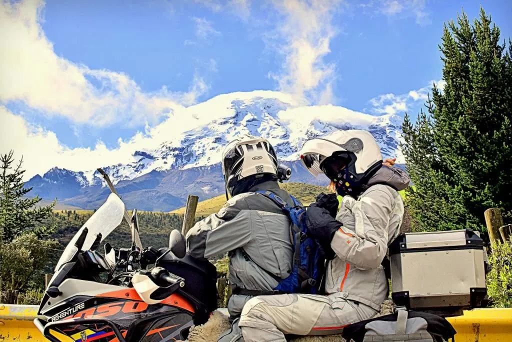 a couple riding an adventure motorcycle with a snow capped mountain of Ecuador in the background